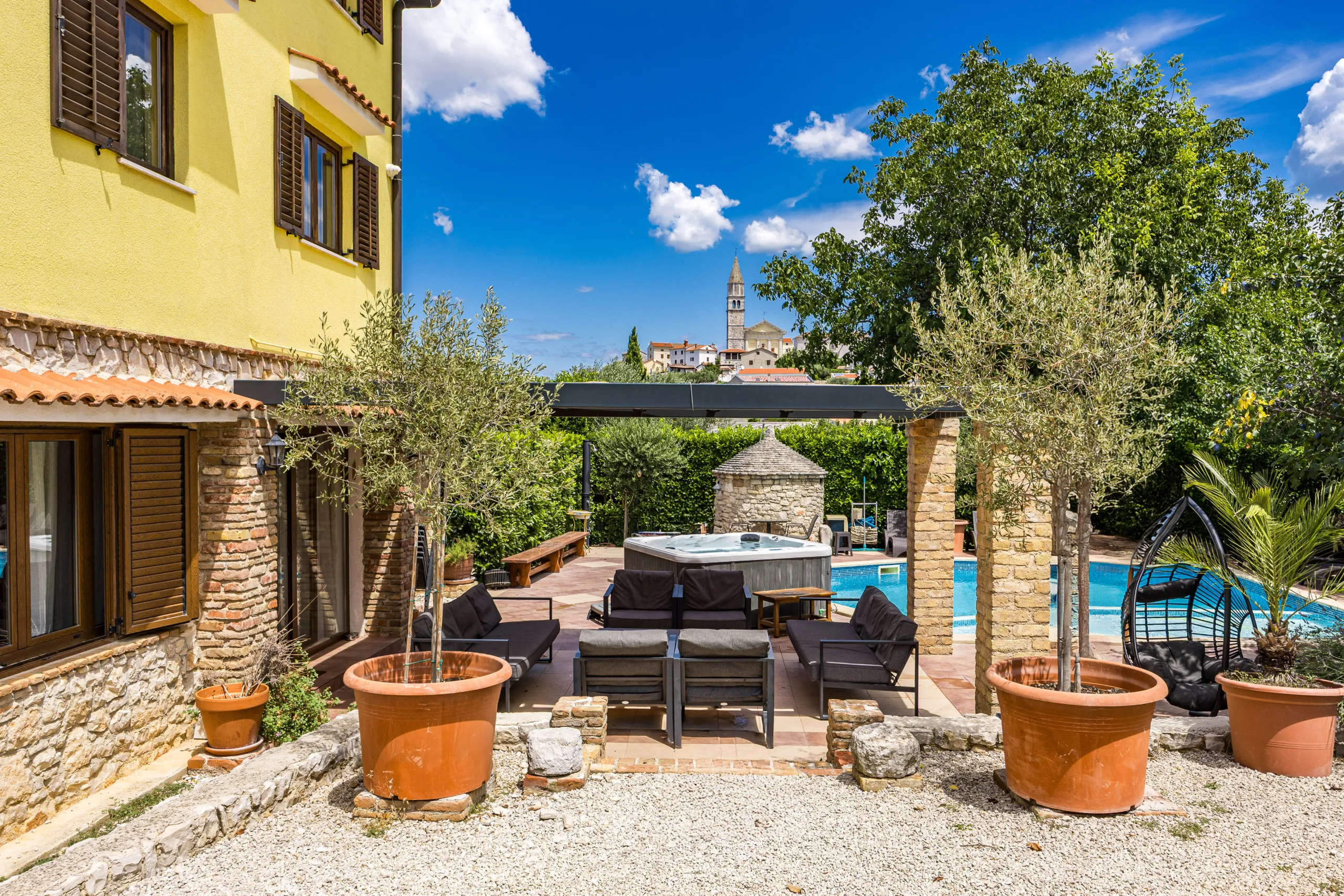 Stone terrace under the pergola with outdoor lounge seating and the hot tub beyond