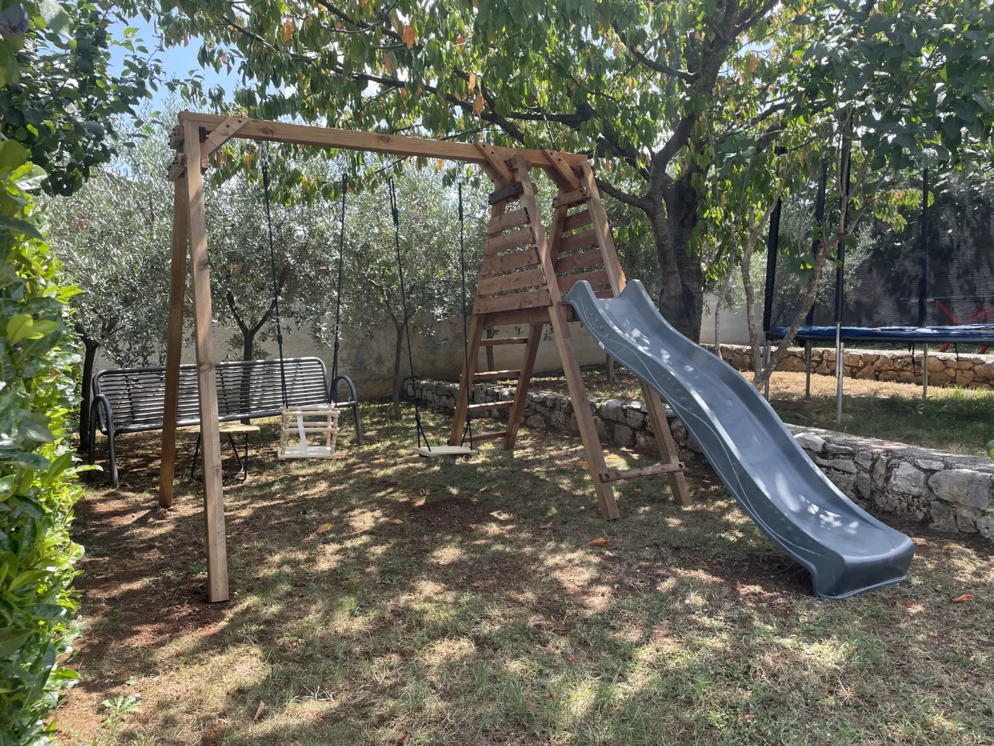 The children's playground with a slide and swing set under the garden trees