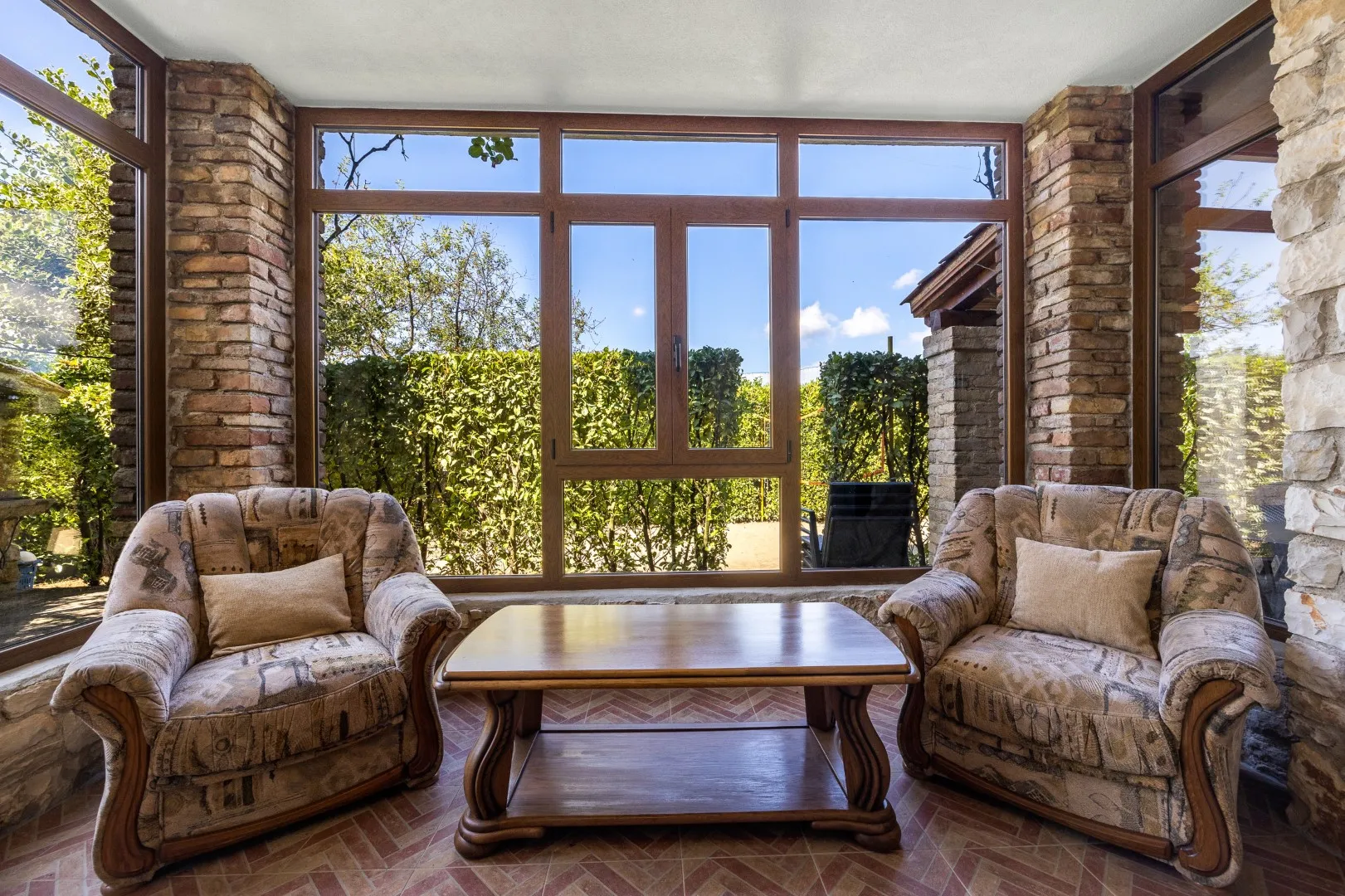 Der Wintergarten aus Backstein und Glas, zwei Sessel mit Blick auf Hecke und Garten