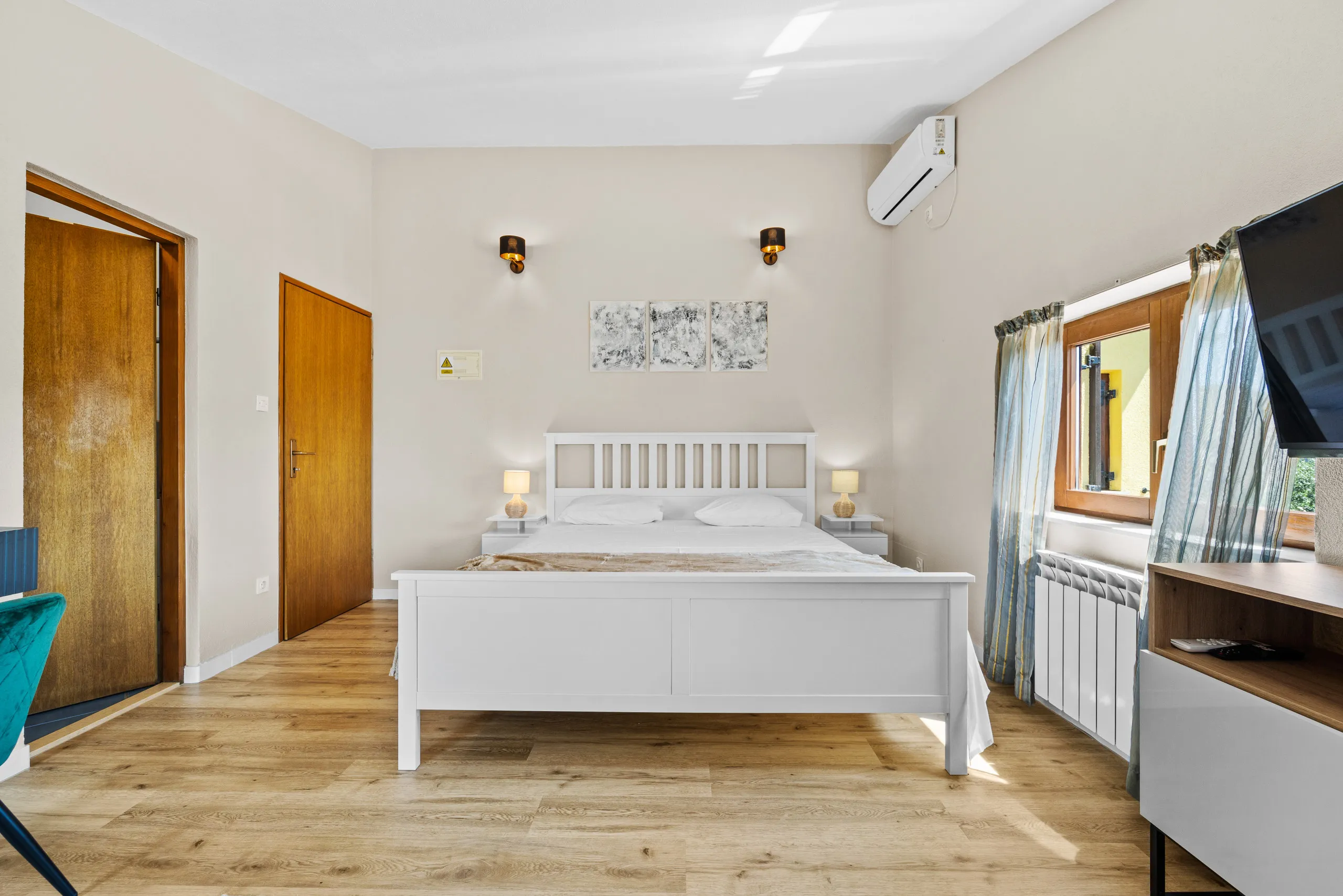 Ein Doppelzimmer mit Wandleuchten, gerahmten Drucken über dem Bett und Fenster zum Garten