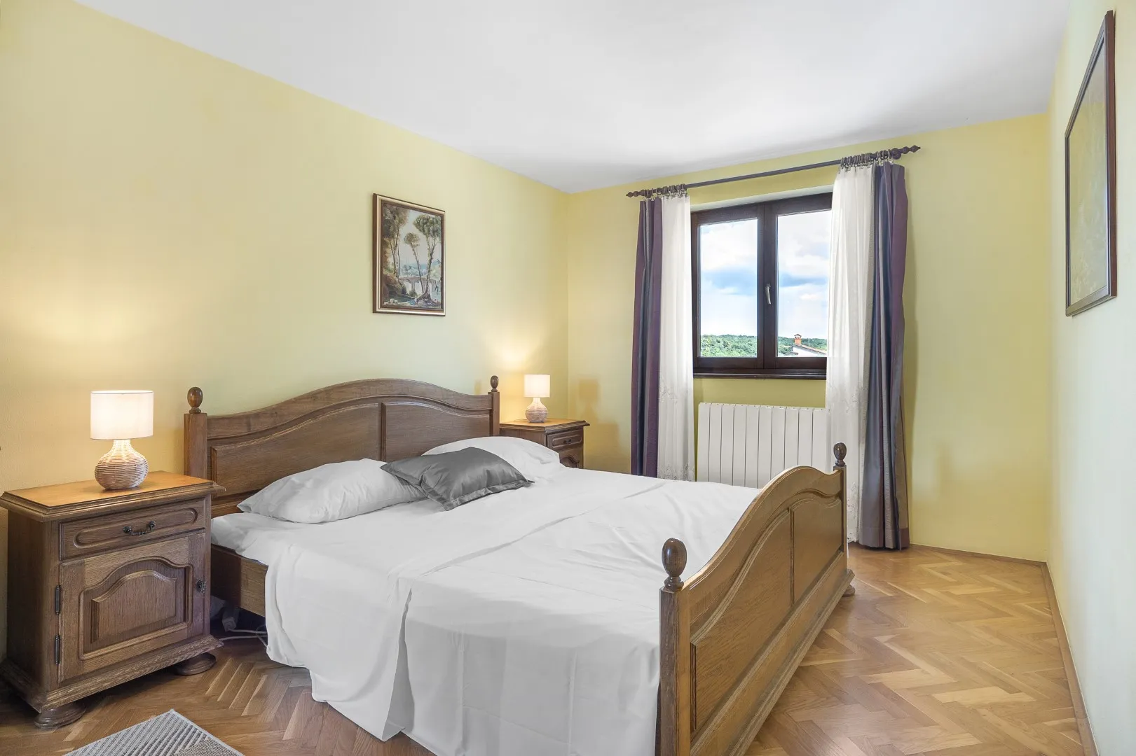 Ein Doppelzimmer mit hellgelben Wänden, geschnitztem Eichenbett und Parkettboden