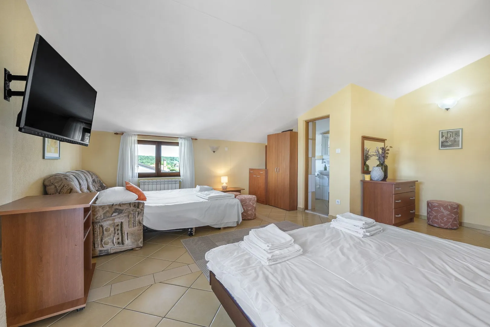 Ein großes Zimmer mit zwei Doppelbetten, Fliesenboden und eigenem Bad hinter der Tür