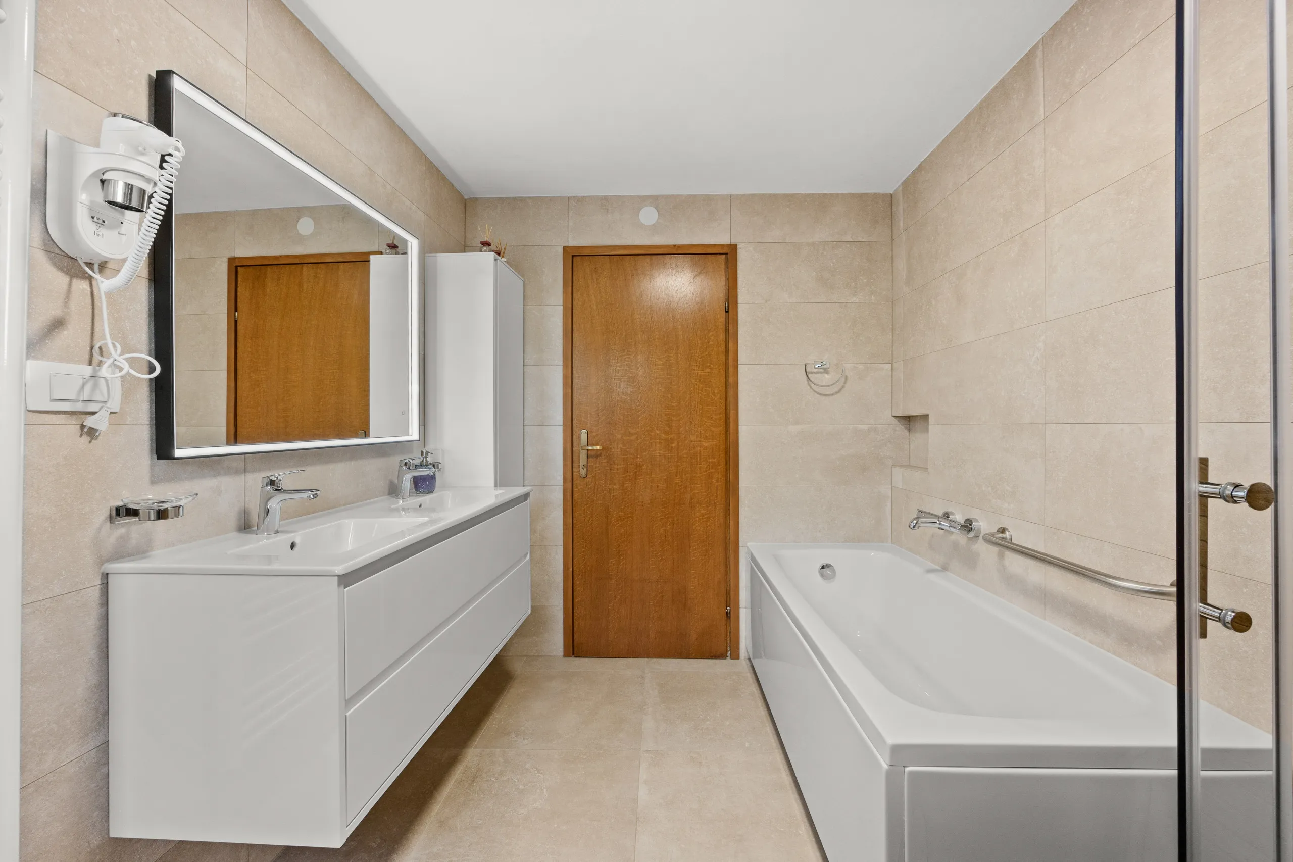 Ein langes Badezimmer mit Doppelwaschtisch und einer Wanne an der Stirnwand